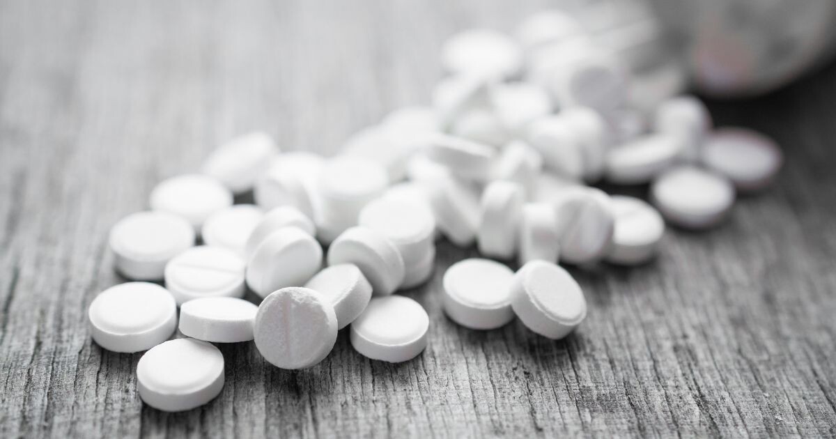 White pills spilled from a bottle onto a wooden surface, illustrating the conversation around cannabis as harm reduction in addressing opioid-related risks
