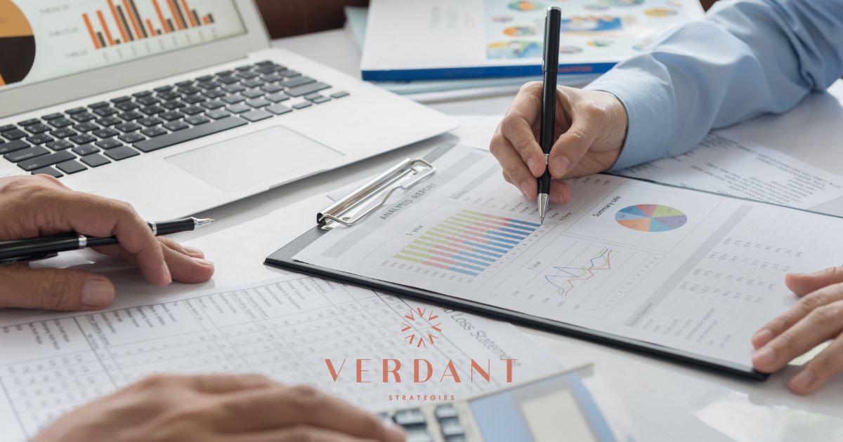 Overhead view of a financial meeting with two individuals analyzing charts and reports labeled 'Analysis Report' and 'Summary Sale,' alongside a laptop displaying graphs, representing cannabis business strategy planning by Verdant Strategies