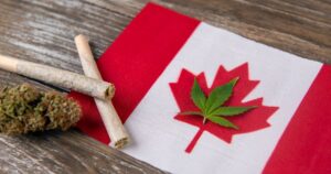 Canadian flag with a cannabis leaf placed on the maple leaf, alongside pre-rolled joints and a cannabis bud on a wooden surface, symbolizing the Canada cannabis industry's role in driving economic growth