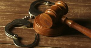Metal handcuffs and a wooden judge's gavel on a rustic wooden surface, symbolizing CannaVibes' efforts in supporting cannabis expungement and justice reform