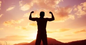 Silhouette of a man flexing his muscles against a vibrant sunset sky, symbolizing strength, wellness, and empowerment for International Men's Day