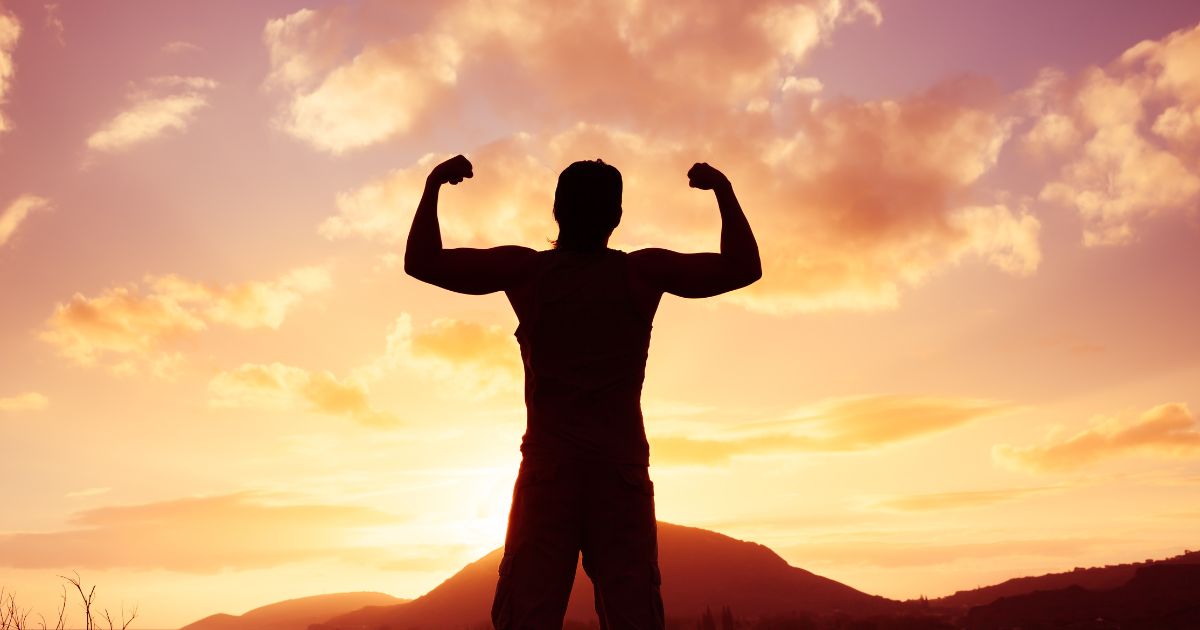 Silhouette of a man flexing his muscles against a vibrant sunset sky, symbolizing strength, wellness, and empowerment for International Men's Day