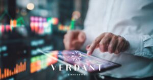 Close-up of hands interacting with a digital tablet displaying colorful data visualizations, set against a blurred background of analytical dashboards, with the Verdant Strategies logo, symbolizing data-driven insights for cannabis operators.