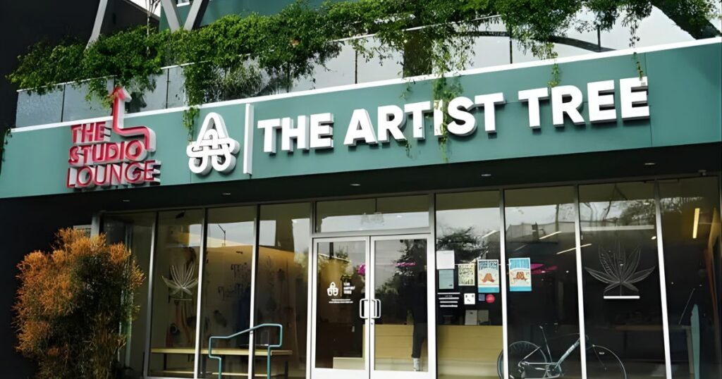 Exterior of The Artist Tree cannabis lounge in WeHo, featuring modern architecture with large glass windows, vibrant greenery, and bold signage for The Studio Lounge and The Artist Tree