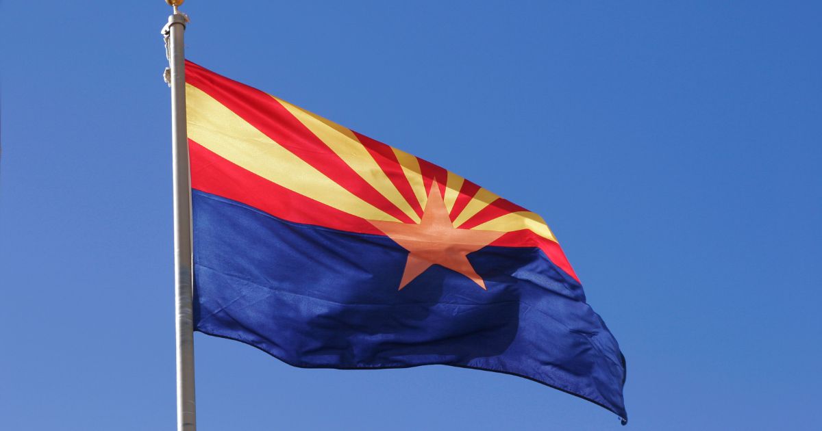 Arizona state flag waving against a clear blue sky, featuring red and gold rays, a copper star, and a dark blue field, symbolizing the debate surrounding the proposed repeal of Arizona's adult-use cannabis legalization