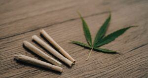 Close-up of four pre-rolled joints and a vibrant green cannabis leaf arranged on a wooden surface. The image evokes the concept of Massachusetts cannabis consumption lounges, highlighting a relaxed and natural setting for enjoying cannabis products