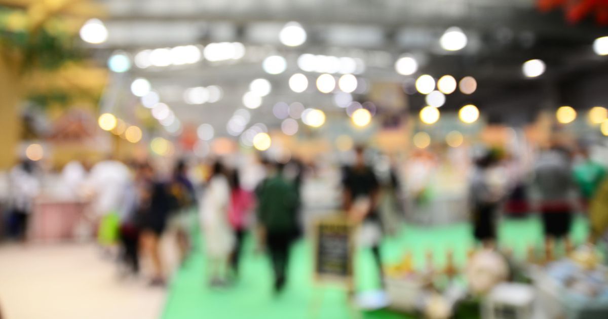 Blurred image of a bustling cannabis event with indistinct human figures, bright bokeh lights, and a green pathway, evoking the lively atmosphere of an indoor gathering