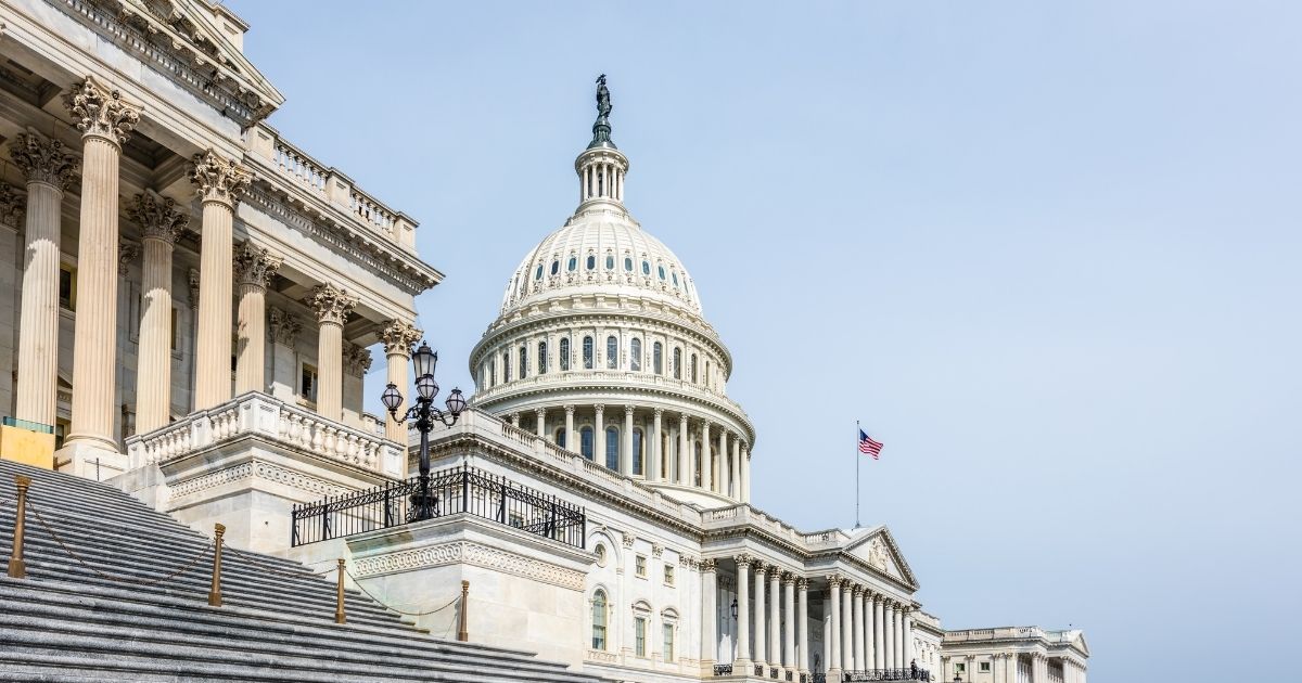 Low-angle view of the United States Capitol Building under a clear blue sky, with its iconic dome and American flag flying, symbolizing legislative progress on federal rescheduling of medical cannabis