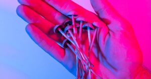 Close-up of a hand holding a cluster of small psilocybin mushrooms, illuminated by dramatic blue and magenta lighting, symbolizing New Jersey's psilocybin therapy pilot program