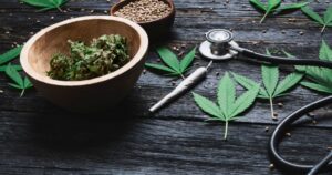 Flat lay image featuring cannabis buds, seeds, and leaves alongside a stethoscope and a rolled joint on a dark wooden surface, symbolizing nursing associations' support for cannabis rescheduling and its medical applications.