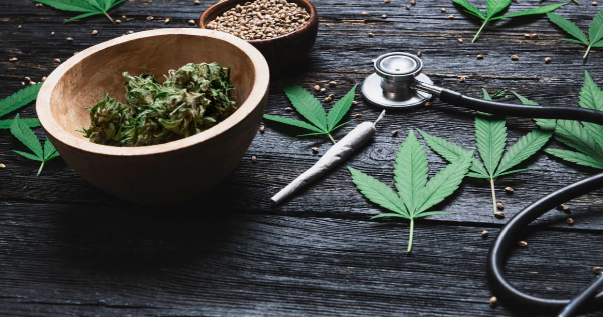 Flat lay image featuring cannabis buds, seeds, and leaves alongside a stethoscope and a rolled joint on a dark wooden surface, symbolizing nursing associations' support for cannabis rescheduling and its medical applications.