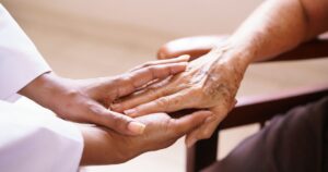 Close-up of a younger hand gently holding an older hand, symbolizing care and support, set against a soft, blurred background, representing the compassionate use of cannabis for terminally ill patients in Virginia.