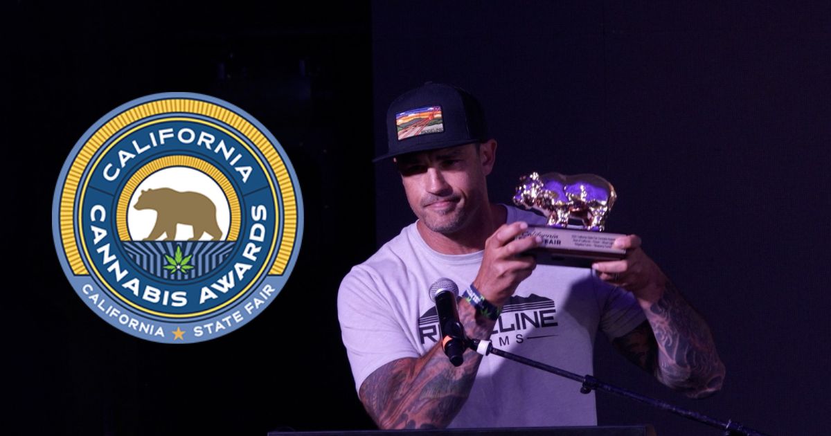 Image of a man holding a golden trophy featuring two bear figures at the California Cannabis Awards 2026. He wears a 'Ridgeline Farms' t-shirt and a black cap with a landscape patch, standing behind a microphone. A circular logo for the California Cannabis Awards and State Fair, with a bear and cannabis leaf, is prominently displayed on the left against a dark event backdrop