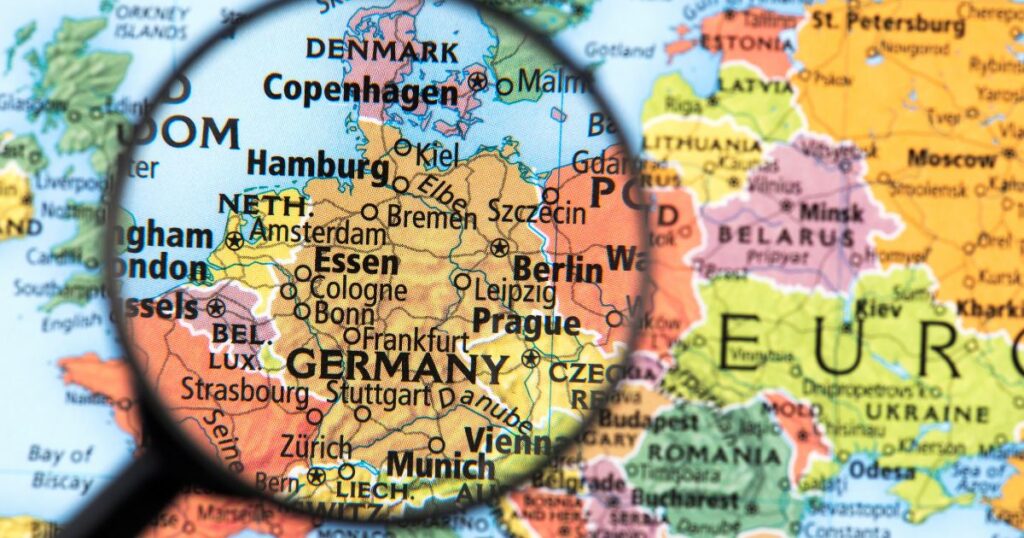 Close-up of a political map of Europe with a magnifying glass centered on Germany, highlighting cities like Berlin, Munich, and Hamburg. The image symbolizes the focus on Germany's cannabis industry and the Organigram-Sanity Group acquisition, emphasizing the region's growing significance in the cannabis market