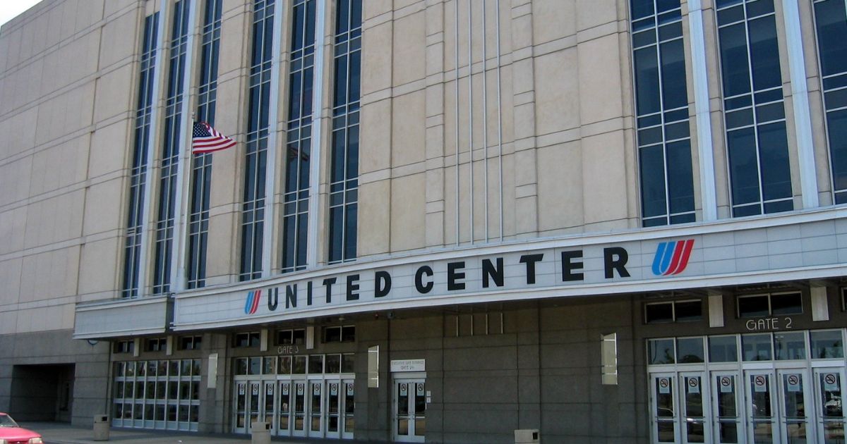 Exterior view of the United Center with prominent signage, glass entrance doors labeled Gate 2 and Gate 3, and an American flag waving, symbolizing its milestone as the first major U.S. arena to serve THC beverages
