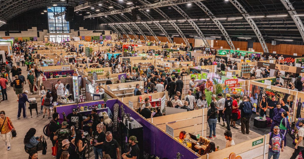 Wide-angle view of a bustling indoor trade show featuring vendor booths, branded banners, and a diverse crowd engaging with exhibits, highlighting the impact of cannabis event sponsorship strategies in a vibrant industry setting.