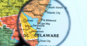 Close-up of a map section focused on Delaware, viewed through a magnifying glass. The magnified area highlights cities like Dover, Milford, and Georgetown, along with Delaware Bay and major highways such as Route 13 and 113. Surrounding regions of Maryland and southern New Jersey are partially visible. Keywords: Ryan's Law Delaware