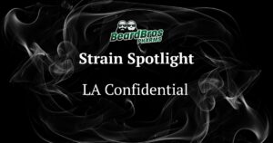 Promotional graphic for BeardBros Pharms featuring the LA Confidential cannabis strain. The design includes a black background with swirling white and grey smoke patterns. At the top, the BeardBros Pharms logo showcases two cartoon-style bearded figures with sunglasses, accompanied by green stylized text. Below the logo, the text 'Strain Spotlight' is prominently displayed, followed by 'LA Confidential' in bold white serif font. The smoky background enhances the cannabis theme. Keywords: LA Confidential cannabis strain