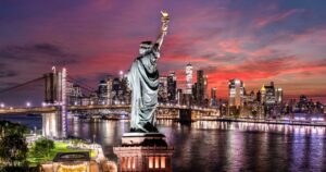 Panoramic view of the New York City skyline at dusk, featuring the Statue of Liberty in the foreground with its torch glowing brightly. symbolizing New York tack and trace cannabis Metrc