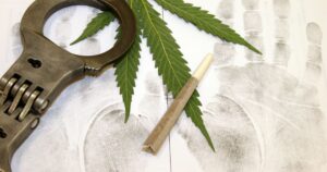 Conceptual image representing cannabis enforcement in the US, featuring a vibrant green cannabis leaf, a rolled joint, and metallic handcuffs placed on a white background covered with black forensic palm and fingerprints, symbolizing the intersection of marijuana use and law enforcement
