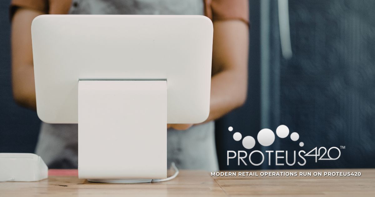 A sleek white point-of-sale system sits on a light wooden countertop, with a blurred retail employee in the background wearing a light-colored apron. The dark background contrasts with the bright 'PROTEUS 420' logo and tagline in the bottom right corner, emphasizing modern retail operations powered by Proteus420