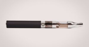 Minimalist product image of a sleek cannabis vape pen featuring a matte black cylindrical body, polished chrome connectors, a transparent tank with amber liquid, and a tapered chrome mouthpiece. The device is centered on a clean, light gray background, emphasizing its modern design