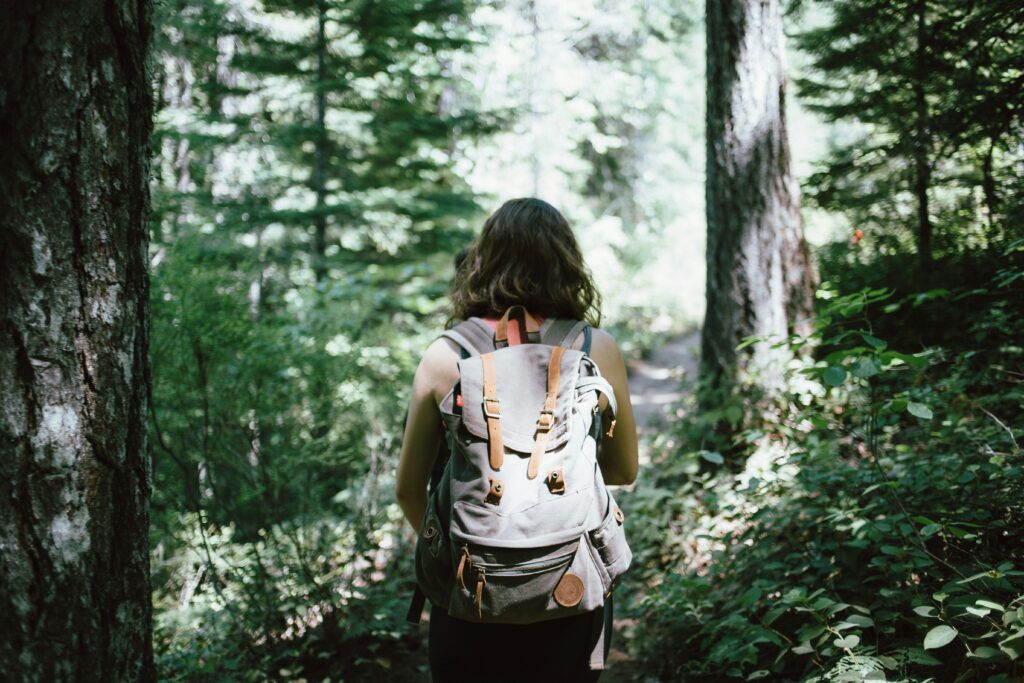 A lady walking on a trail through the woods.