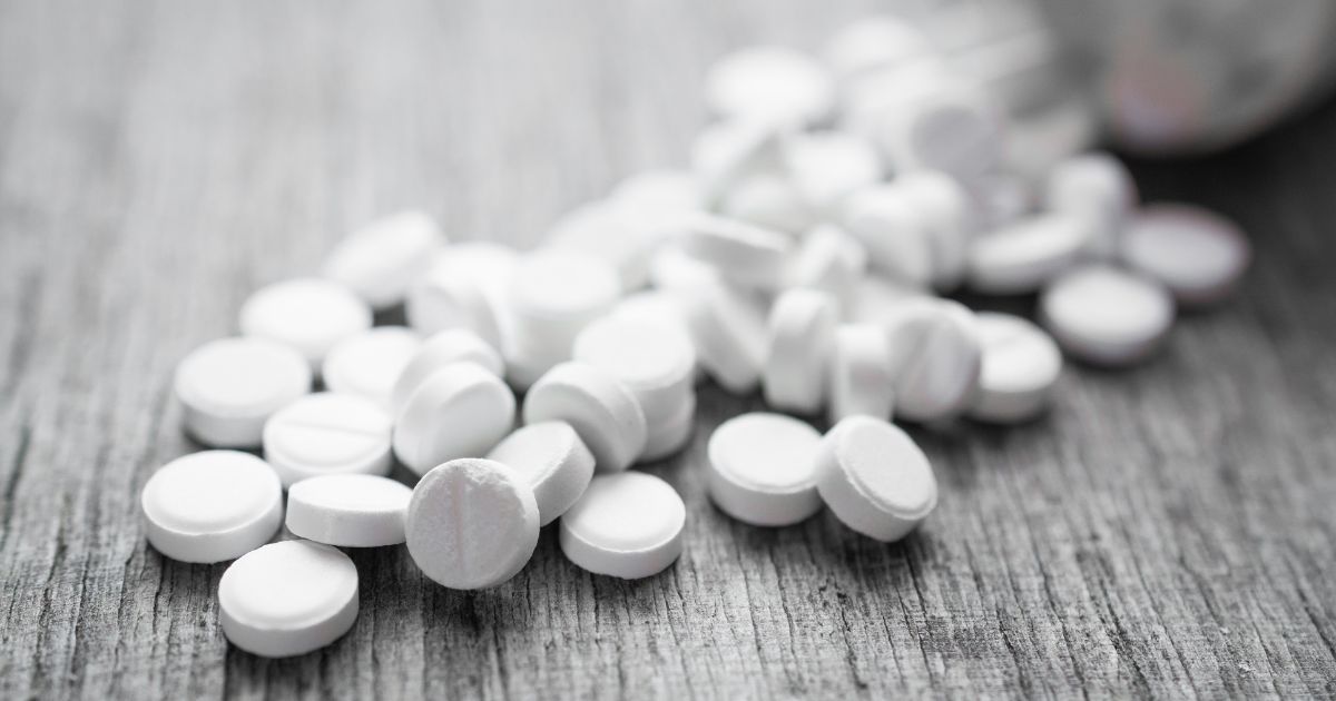 White pills spilled from a bottle onto a wooden surface, illustrating the conversation around cannabis as harm reduction in addressing opioid-related risks