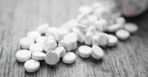 White pills spilled from a bottle onto a wooden surface, illustrating the conversation around cannabis as harm reduction in addressing opioid-related risks