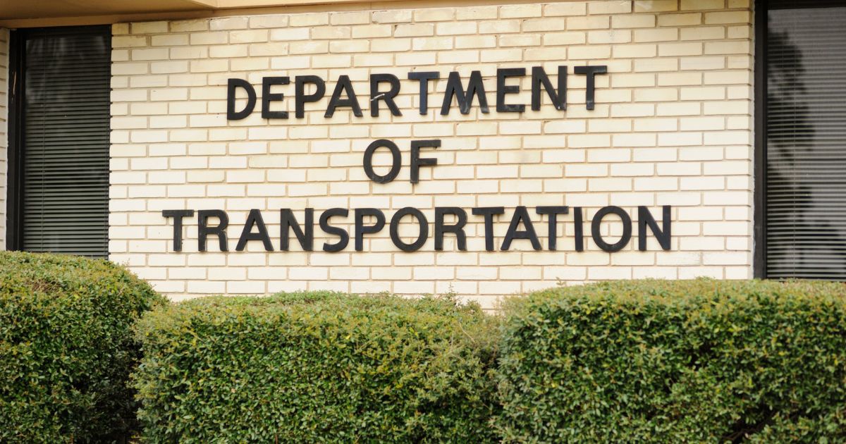 Department of Transportation sign on a light brick wall above green bushes, a focal point for DOT medical cannabis news.