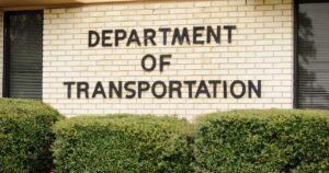 Department of Transportation sign on a light brick wall above green bushes, a focal point for DOT medical cannabis news.