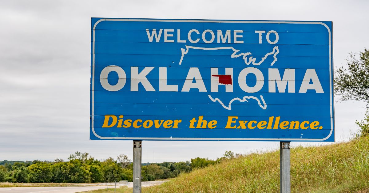 Welcome to Oklahoma highway sign with the state highlighted in red on a U.S. map, photographed beside a roadside embankment under a gray sky to represent Oklahoma medical marijuana policy.