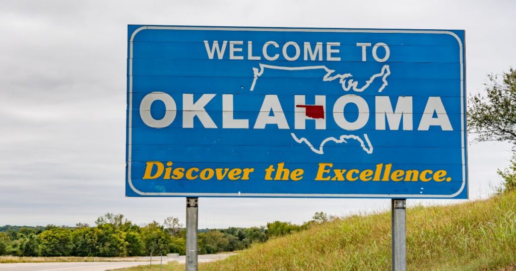 Welcome to Oklahoma highway sign with the state highlighted in red on a U.S. map, photographed beside a roadside embankment under a gray sky to represent Oklahoma medical marijuana policy.