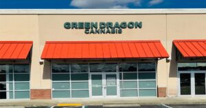 Green Dragon Yulee dispensary storefront in a suburban strip mall, featuring bright orange awnings, large green “GREEN DRAGON CANNABIS” signage, frosted glass windows, and a central entrance under a blue sk