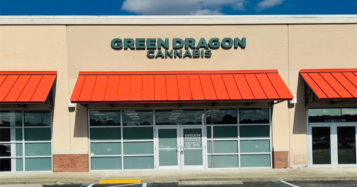 Green Dragon Yulee dispensary storefront in a suburban strip mall, featuring bright orange awnings, large green “GREEN DRAGON CANNABIS” signage, frosted glass windows, and a central entrance under a blue sk