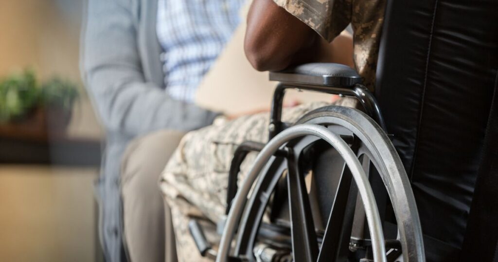 A person in military camouflage and a wheelchair consults with someone holding a folder regarding veterans medical marijuana.