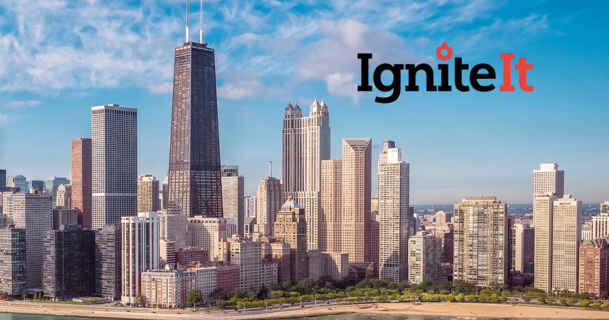 Chicago skyline with 875 North Michigan Avenue, surrounding high-rises, beach, and lakefront under a clear blue sky, featuring the IgniteIt Chicago logo in the upper right.